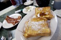 Close up of French toasts and bacon on restaurant table — Stock Photo