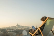 Мужчина отдыхает на террасе на крыше с цифровым планшетом — стоковое фото