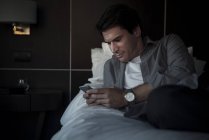 Мужчина отдыхает на кровати с мультимедийным смартфоном — стоковое фото