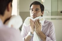 Чоловік дивиться у дзеркало, сушить обличчя рушником — стокове фото