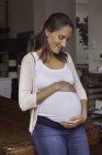 Портрет беременной женщины, держащейся за руки на животе дома — стоковое фото