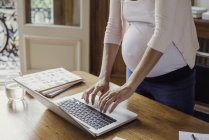 Mujer embarazada usando ordenador portátil - foto de stock