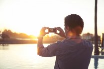 Homme photographiant coucher de soleil avec smartphone — Photo de stock