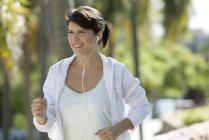 Woman jogging outdoors listening music in earphones — Stock Photo