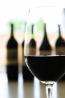 Крупним планом склянка червоного вина і пляшок вина на фоні — стокове фото