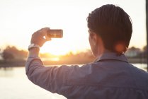 Чоловік фотографує захід сонця зі смартфоном — стокове фото