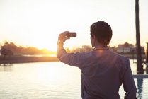 Hombre fotografiando puesta de sol con smartphone - foto de stock