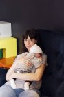 Мати тримає сплячого немовляти, сидячи на дивані — стокове фото