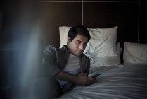 Мужчина отдыхает на кровати со смартфоном — стоковое фото