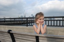 Kleines Mädchen, das auf einem Pier mit New Yorker Wolkenkratzern im Hintergrund ruht, New York, USA — Stockfoto