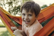Портрет улыбающегося мальчика, сидящего в гамаке на открытом воздухе — стоковое фото