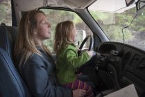 Menina sentada no colo da mãe atrás do volante do carro — Fotografia de Stock