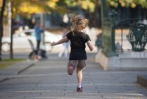 Rückansicht eines kleinen Mädchens, das auf dem Gehweg läuft — Stockfoto