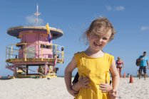 Маленькая девочка на пляже с младшим братом, прячущимся за ней — стоковое фото