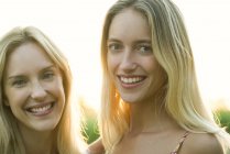 Retrato de dos mujeres rubias sonriendo en la cámara al aire libre - foto de stock