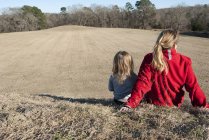 Заднього вигляду мати і дочка сидять разом на пагорбі — стокове фото