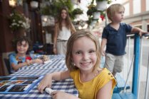 Retrato de menina sentada no café ao ar livre com irmãos e mãe — Fotografia de Stock