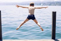 Visão traseira do menino pulando no lago — Fotografia de Stock