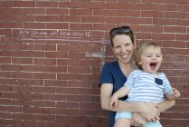 Портрет матери и сына малыша, стоящих вместе на фоне кирпичной стены на улице — стоковое фото