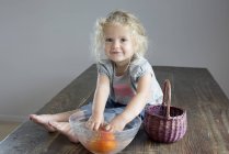 Девушка полоскает овощи в миску, сидя на деревянном столе — стоковое фото