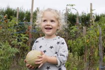 Portrait of little girl holding cantaloupe in garden — Stock Photo