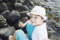 Boy wearing hat sitting by stream — Stock Photo