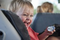 Menino criança rindo no carro e segurando chupeta na mão — Fotografia de Stock
