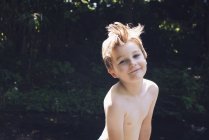 Porträt eines Jungen mit nacktem Oberkörper, der in die Kamera blickt, mit Fluss im Hintergrund — Stockfoto