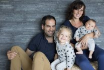 Портрет сім'ї з двома маленькими дітьми, що сидять на ліжку вдома — стокове фото