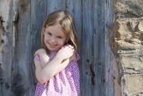 Porträt des niedlichen lächelnden kleinen Mädchens, das an der Holztür steht — Stockfoto