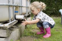 Petite fille se lave les mains sous le robinet extérieur de la citerne — Photo de stock