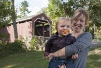 Portrait of Mother holding toddler son in front of covered bridge — Stock Photo