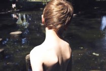 Vue arrière du garçon à poitrine nue debout au bord de l'eau — Photo de stock