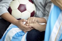 Visão cortada de crianças e adultos de mãos dadas e bola de futebol — Fotografia de Stock