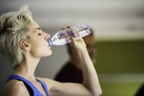 Жінка п'є воду з пляшки під час тренувань на біговій доріжці — стокове фото