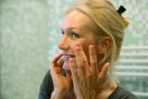 Reife Frau untersucht Gesicht im Spiegel — Stockfoto