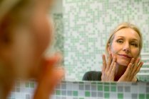 Reife Frau untersucht ihr Gesicht im Badezimmerspiegel — Stockfoto