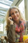 Зріла жінка розмовляє на мобільний телефон і посміхається в кафе — стокове фото