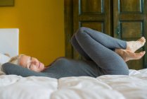 Donna matura sdraiata sul letto con le ginocchia al petto — Foto stock
