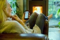 Зріла жінка розслабляється вдома зі смартфоном — стокове фото