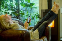 Зріла жінка сміється, розслабляючись вдома зі смартфоном — стокове фото