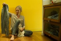 Зріла жінка сидить на підлозі спальні, розмірковуючи про сорочку — стокове фото