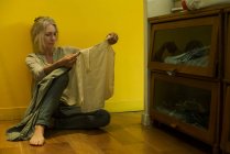 Donna matura seduta sul pavimento a guardare la camicia con espressione infelice — Foto stock