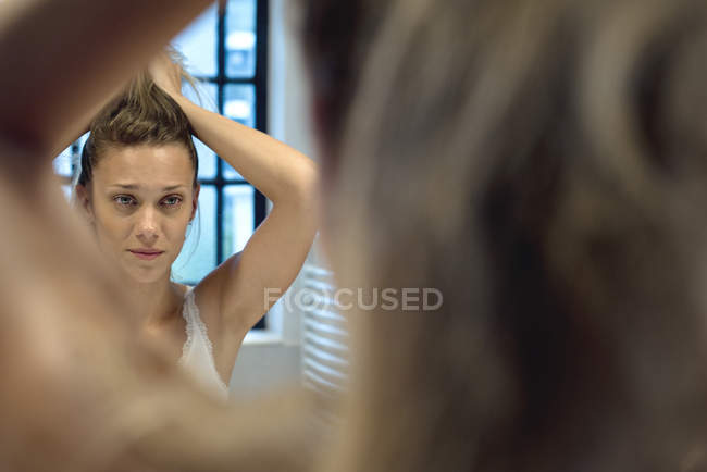 Woman styling hair in bathroom mirror — Stock Photo