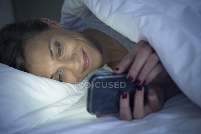 Frau liegt mit Smartphone im Bett — Stockfoto