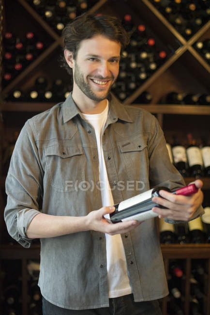 Улыбающийся покупатель выбирает бутылку вина — стоковое фото
