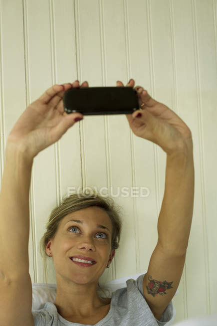 Женщина делает селфи на смартфоне в кровати — стоковое фото