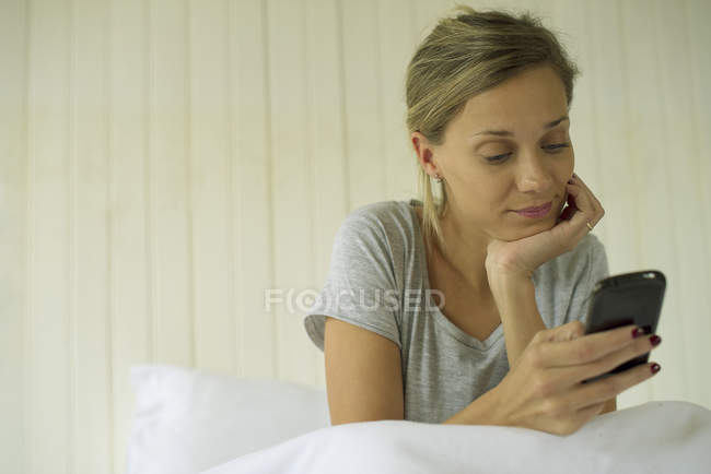 Donna seduta a letto con smartphone — Foto stock