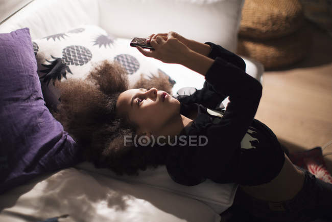 Chica reclinada contra el sofá, absorta en el teléfono inteligente - foto de stock