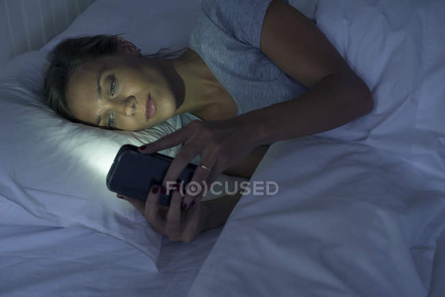 Donna sdraiata a letto con smartphone — Foto stock